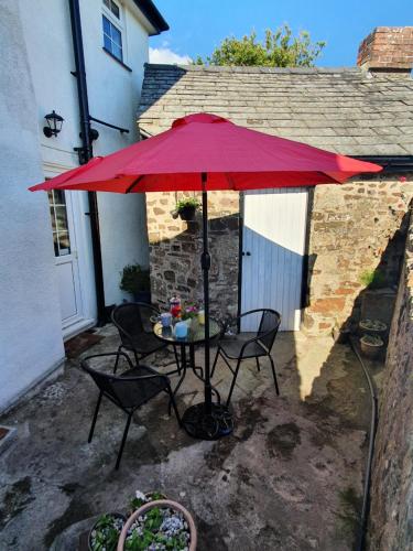 a table and chairs under a red umbrella at Boots Cottage in Bude