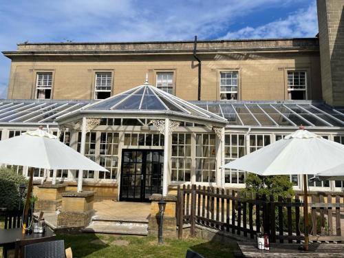 a building with a greenhouse and two umbrellas in front of it at Manor Hotel by Greene King Inns in Yeovil