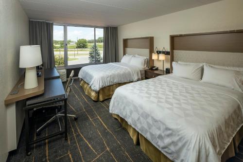a hotel room with two beds and a desk and a window at Holiday Inn Detroit Lakes by IHG in Detroit Lakes