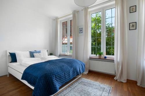 a white bedroom with a bed and two windows at Elite Apartments Hamptons Old Town in Gdańsk