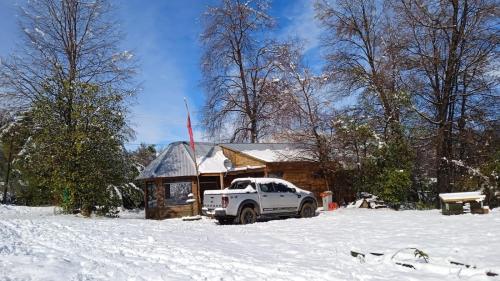 Ein weißer Truck parkt vor einer Hütte im Schnee. in der Unterkunft Cabaña Recinto Valle Las Trancas in Recinto