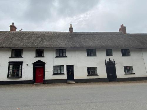 a white building with black windows and a red door at Thatched Cottage, beautiful village near the sea in Otterton