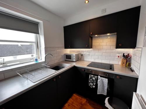 uma cozinha com armários pretos, um lavatório e uma janela em Renfrew Home from Home em Renfrew