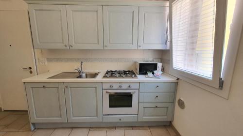 a kitchen with white cabinets and a sink and a window at Appartamento Perla Marina in Sottomarina