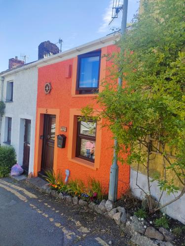 una casa arancione e bianca con un albero di fronte di Fishermen's cottage with log burner, 2 bathrooms & sea views from garden terraces a The Mumbles