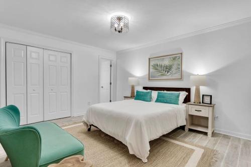 a white bedroom with a bed and a green chair at Lakefront, Saltwater Pool, Backyard Oasis, Private Dock, Home Gym in Flowery Branch
