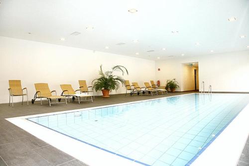 a swimming pool in a room with chairs and tables at Alpenhotel Ammerwald in Reutte