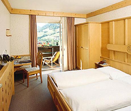 a bedroom with a bed and a desk and a balcony at Hotel Austria in Niederau