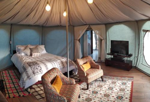 a bedroom with a bed and two chairs and a tv at Glamping ILLARI Boutique in Paipa