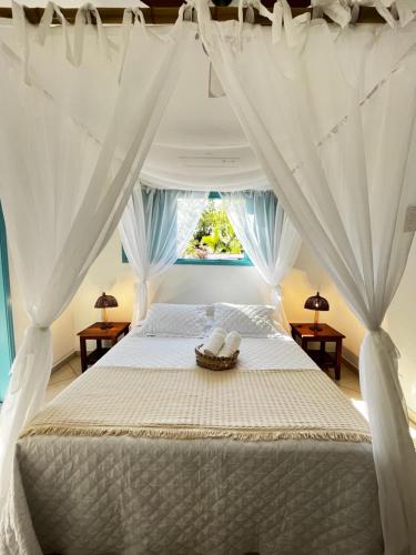 a bedroom with a bed with white curtains and a window at Villa Tiê Paraty in Paraty