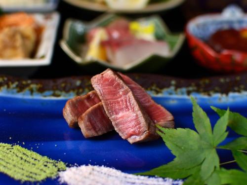 a piece of meat on a blue plate with herbs at Kappo Ryokan Yumesaki in Beppu