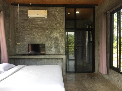 a bedroom with a bed and a tv and a door at ชลลดา ริเวอร์ โฮมสเตย์ แก่งกระจาน in Ban Wang Malako