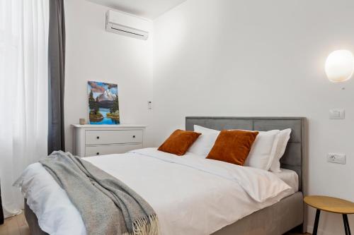 1 dormitorio con 1 cama con sábanas blancas y almohadas de color naranja en VD Boutique Apartments No 1 Bucharest, en Bucarest