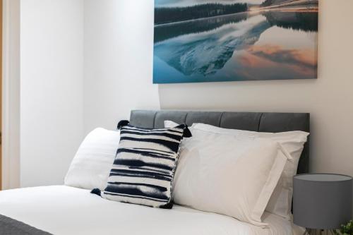 a bed with white pillows and a painting on the wall at Skyvillion - 4 Bed Luxury Apartment with Balcony & Parking in Enfield