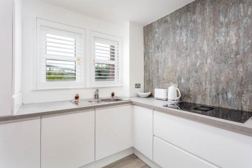 a white kitchen with white cabinets and a window at 9A Millbrae - Donnini Apartments in Ayr