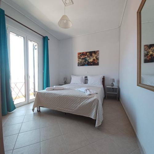 a white bedroom with a bed and a large window at Jerrys Home Agios Petros in Áyios Pétros