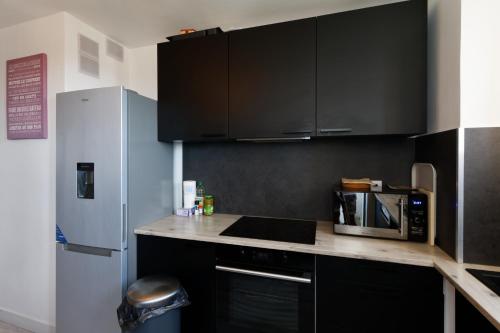 - une cuisine avec des armoires noires et un réfrigérateur dans l'établissement LE BEAULIEU * Appartement 4 chambres * 8pers * Clim * Parking * Balcon, à Montpellier