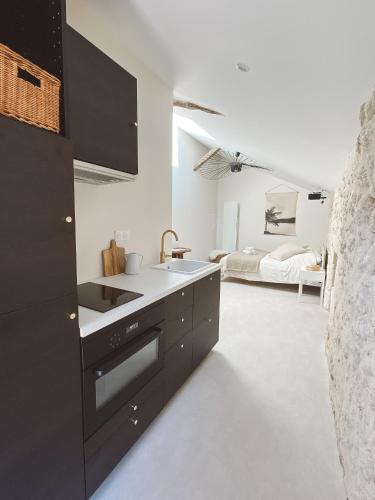 uma cozinha com armários pretos e uma cama ao fundo em La Parenthèse, joli studio avec terrasse em Valeuil