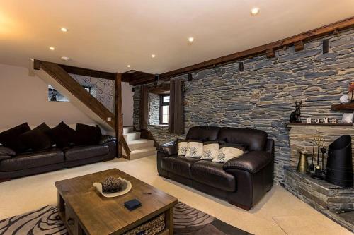 een woonkamer met een leren bank en een stenen muur bij Luxurious Self Catering Holiday Cottage Cornwall in Menheniot