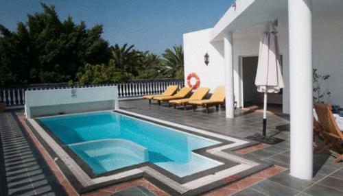 a swimming pool with chairs and an umbrella on a patio at Villas del Mar Viña y Cabrera in Puerto Calero