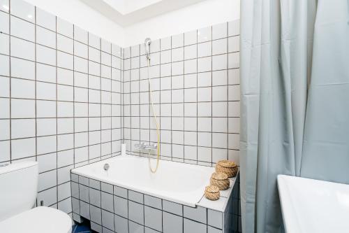 a white tiled bathroom with a tub and a toilet at Cosy Apartment by LoftAffair in Krakow