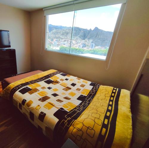 een slaapkamer met een quilt op een bed met een raam bij Zona Sur - Lindo Monoambiente en la Meseta de Achumani - URBEANDINA in La Paz