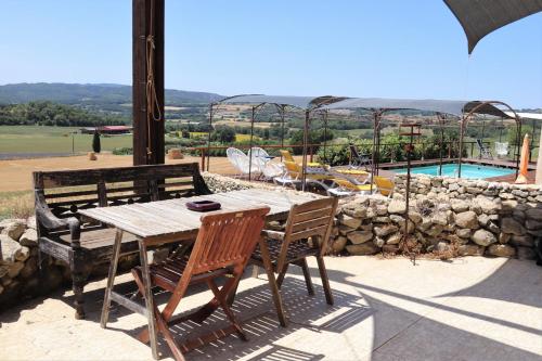 einen Holztisch und Stühle auf einer Terrasse mit einem Pool in der Unterkunft La petite grande in Lurs