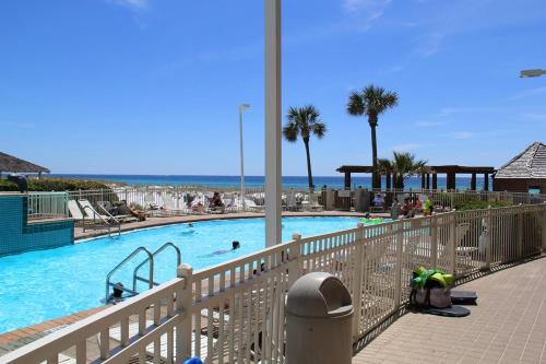 a swimming pool with palm trees and the ocean in the background at Pelican Beach Terrace 805 in Destin