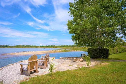 two wooden benches sitting on the shore of a lake at Somewhere In Time - RETRO SPACIOUS COTTAGE with PRIVATE SANDY BEACH in Wiarton