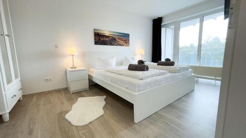 una camera bianca con un grande letto e una grande finestra di Strandhaus-Nordseebrandung-Fewo-B1-2 a Cuxhaven