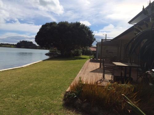 einem Picknicktisch und Bänken neben einem Wasserkörper in der Unterkunft Absolute Waterfront Serenity Near Auckland in Clarks Beach