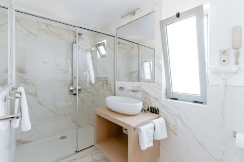 a white bathroom with a sink and a shower at Palm Beach Hotel Apartments in Rethymno Town