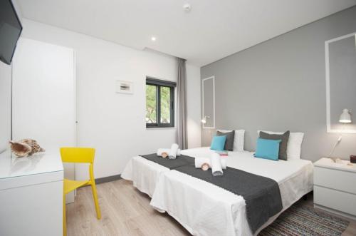 a white bedroom with a bed and a yellow chair at In Downtown - Villa Serenity in Albufeira