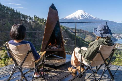 two people sitting in chairs in front of a fireplace at つながるキャンプリゾートQOONEL+ in Fujikawaguchiko