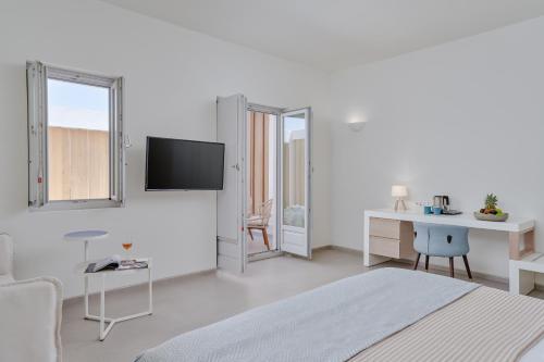a white room with a bed and a desk and a tv at Meltemi Blu - Adults Only in Perissa