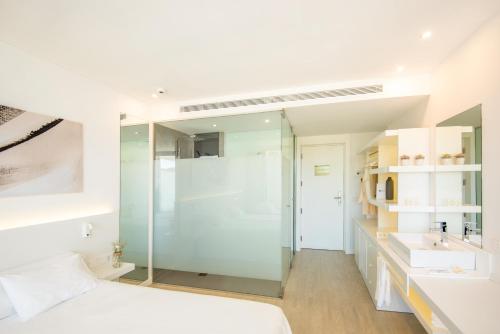 a bathroom with a glass shower and a bed at Els Pins Resort & Spa - Emar Hotels in San Antonio Bay