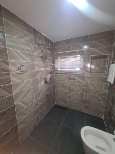 a tiled bathroom with a toilet and a window at Wine House, Maitama, Abuja in Abuja
