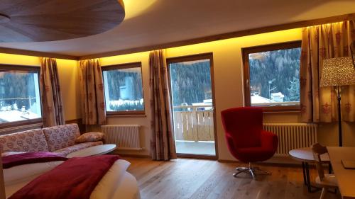 a bedroom with a bed and a chair and windows at Hotel Cesa Tyrol in Canazei