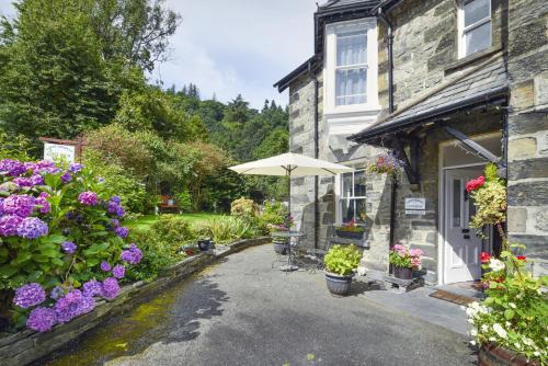 une maison avec un parasol et des fleurs devant elle dans l'établissement Garth Dderwen, à Betws-y-coed