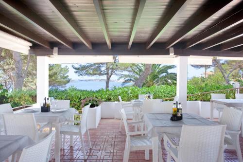 a patio with white tables and white chairs at Apartamentos Club Cala Azul in Cala Llenya
