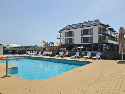 a swimming pool with chairs and a building in the background at Loft Apartamenty w Sarbinowie in Sarbinowo