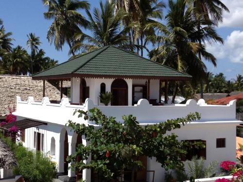 a white house with a green roof and palm trees at Mwendawima Beach Villa in Jambiani