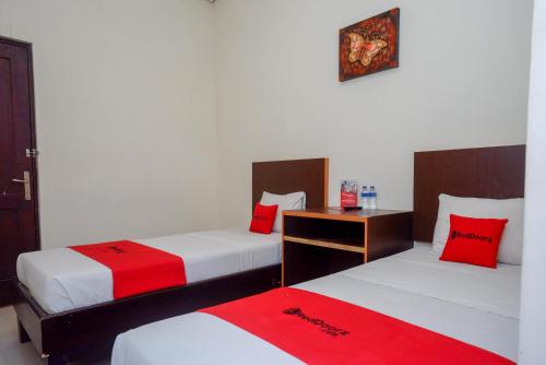 2 camas en una habitación con sábanas rojas y blancas en RedDoorz Syariah At Namira Hotel, en Yogyakarta