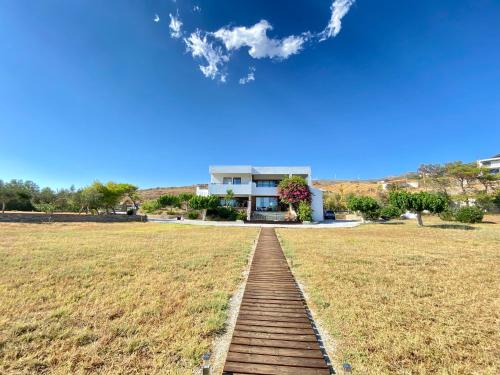 a house on a field with a wooden walkway at Svolis Beachhouse - Villa Set in a Beautiful Bay in Karistos