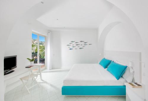 a white bedroom with a blue bed and a tv at Hotel Le Terrazze in Conca dei Marini