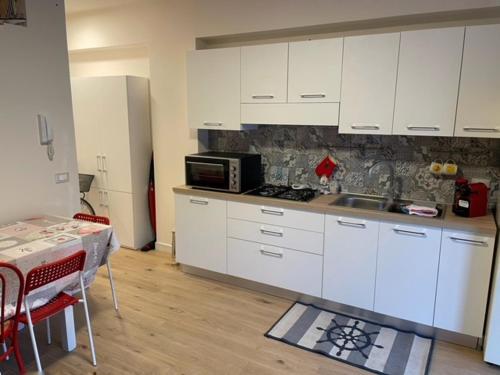 cocina con armarios blancos, mesa y microondas en Incantevole appartamento Taormina, en SantʼAlessio Siculo