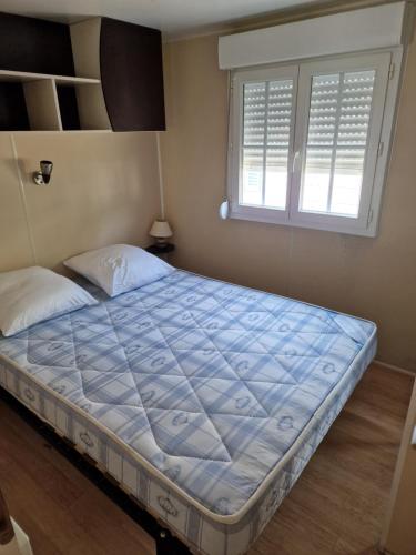 ein großes Bett in einem Schlafzimmer mit Fenster in der Unterkunft Grand Mobile home dans camping in Mimizan
