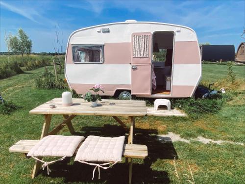 a pink and white caravan with a table and benches at Het Caravannetje B&B - retro glamping in Leidschendam