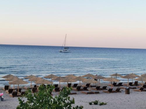 a beach with chairs and umbrellas and a boat in the ocean at Anatolikos Rooms in Alykes