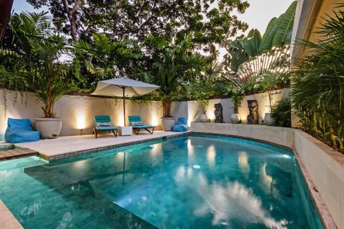 a swimming pool with two chairs and an umbrella at Villa Karang Berawa in Canggu